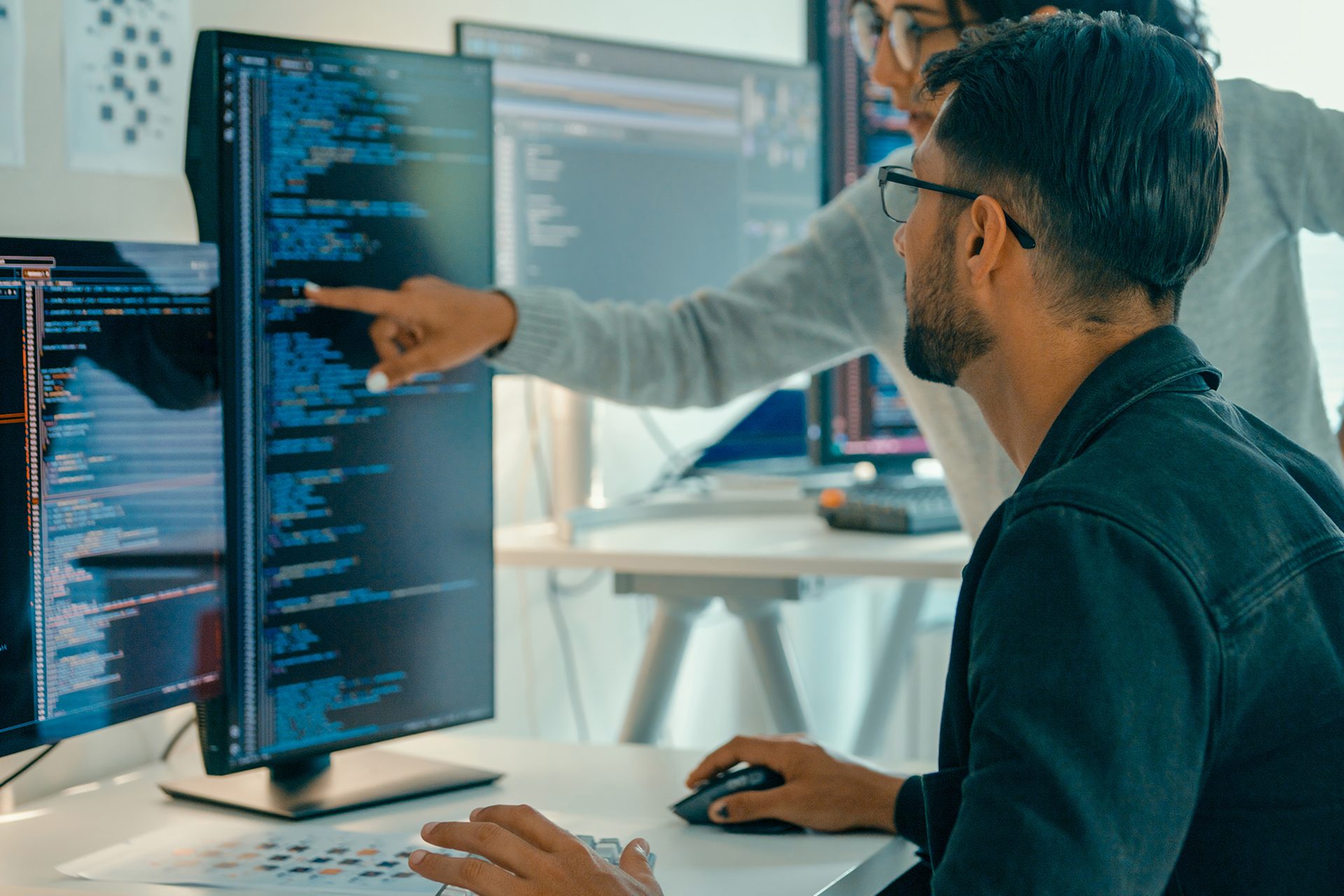 Woman pointing at computer screen of man writing code