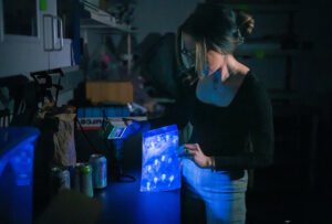 Professor Sarah Bailey holds a UV light, revealing fingerprints on a piece of plastic