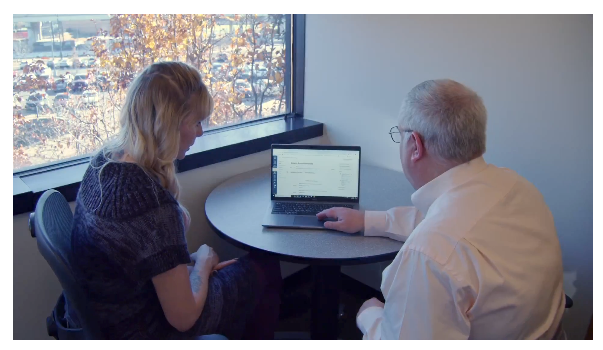 Faculty member with laptop on table getting assistance from support staff member