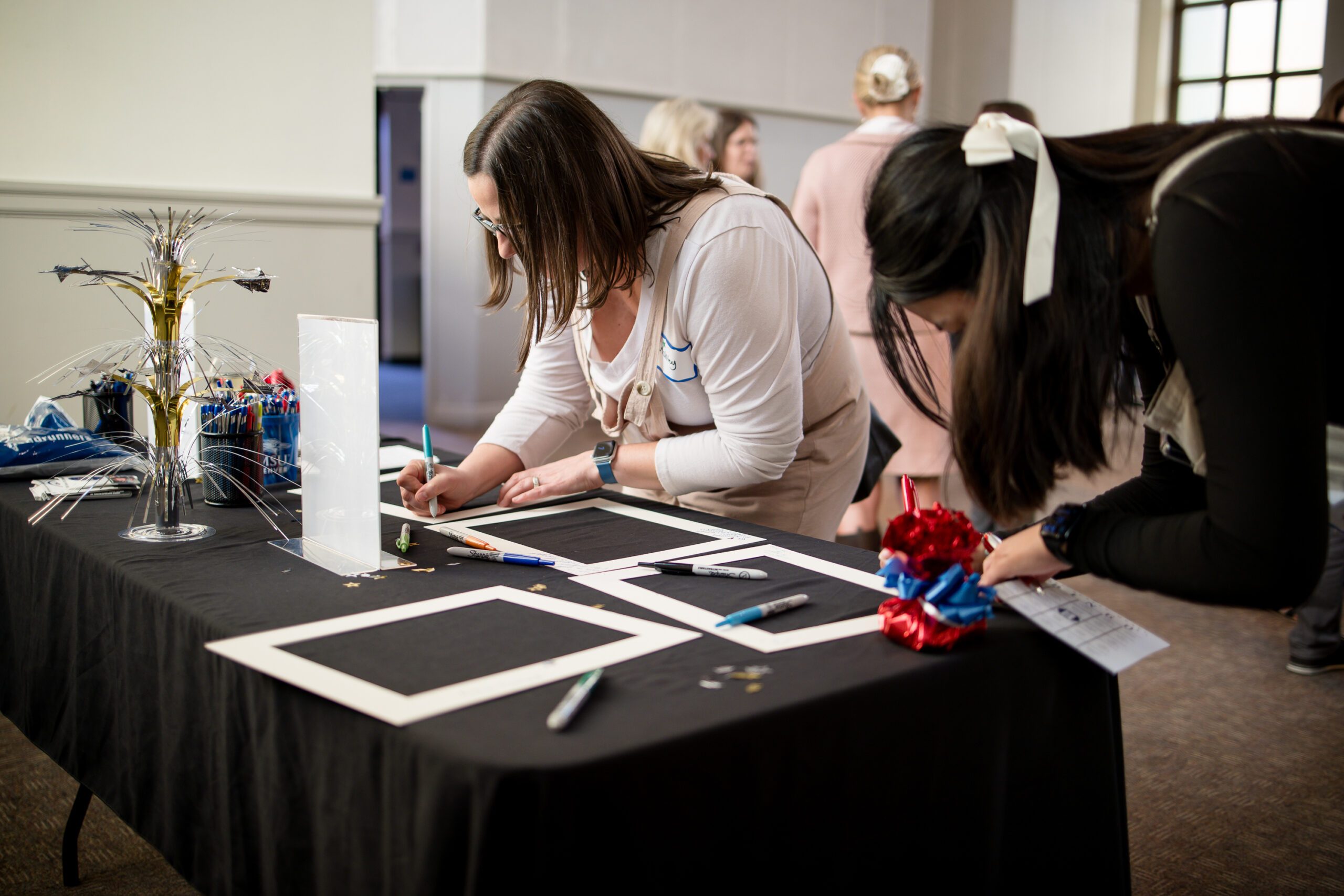 MPAcc's 15 year anniversary - 2 attendees signing photo frame mats at a decorated table
