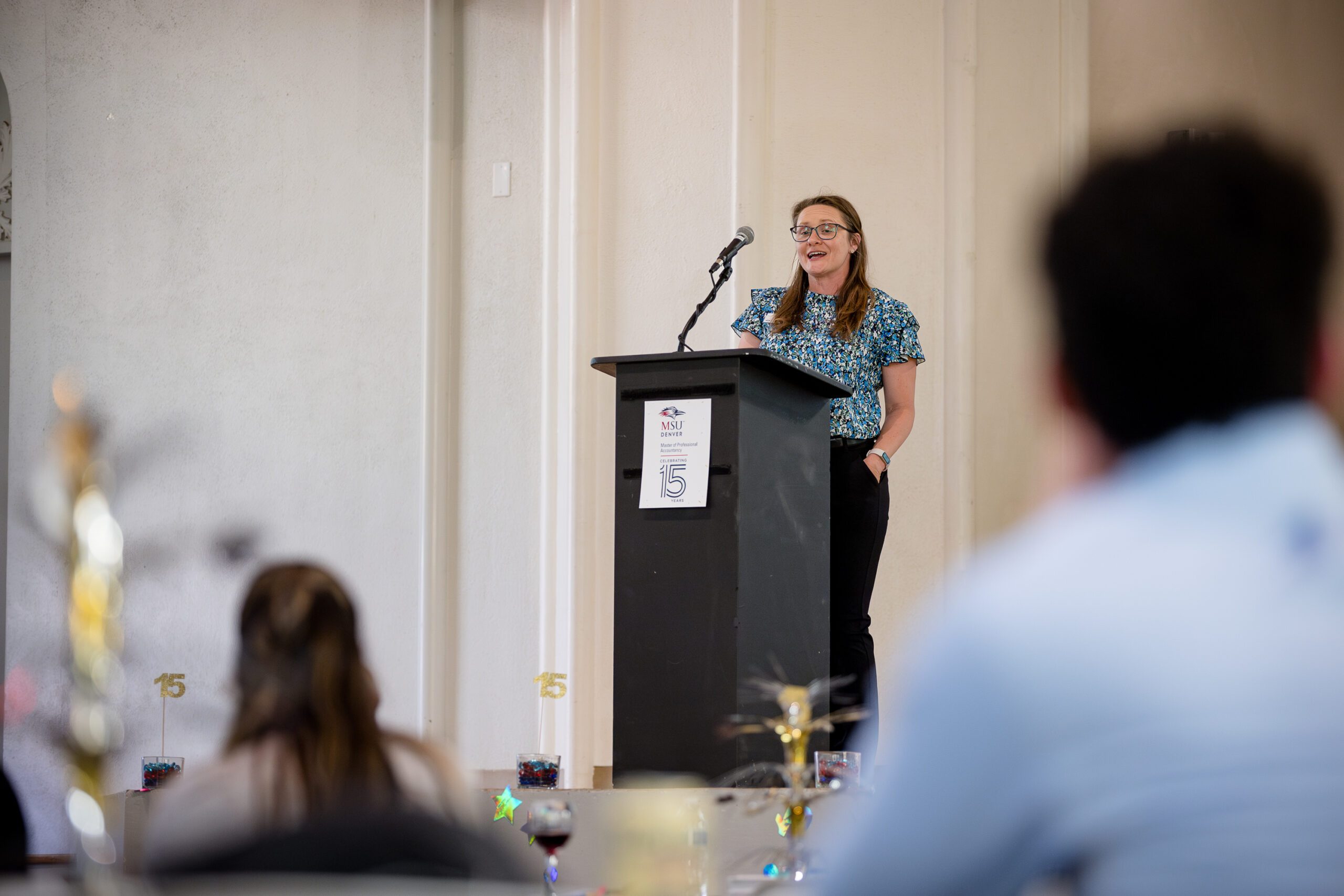 Dr. Letitia Pleis talking on a decorated stage at the podium in front of attendees