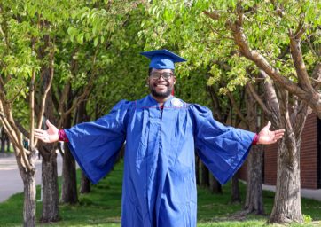 2025 MSU Denver graduate Chrisnel Akele standing in front of trees on campus with his arms spread wide