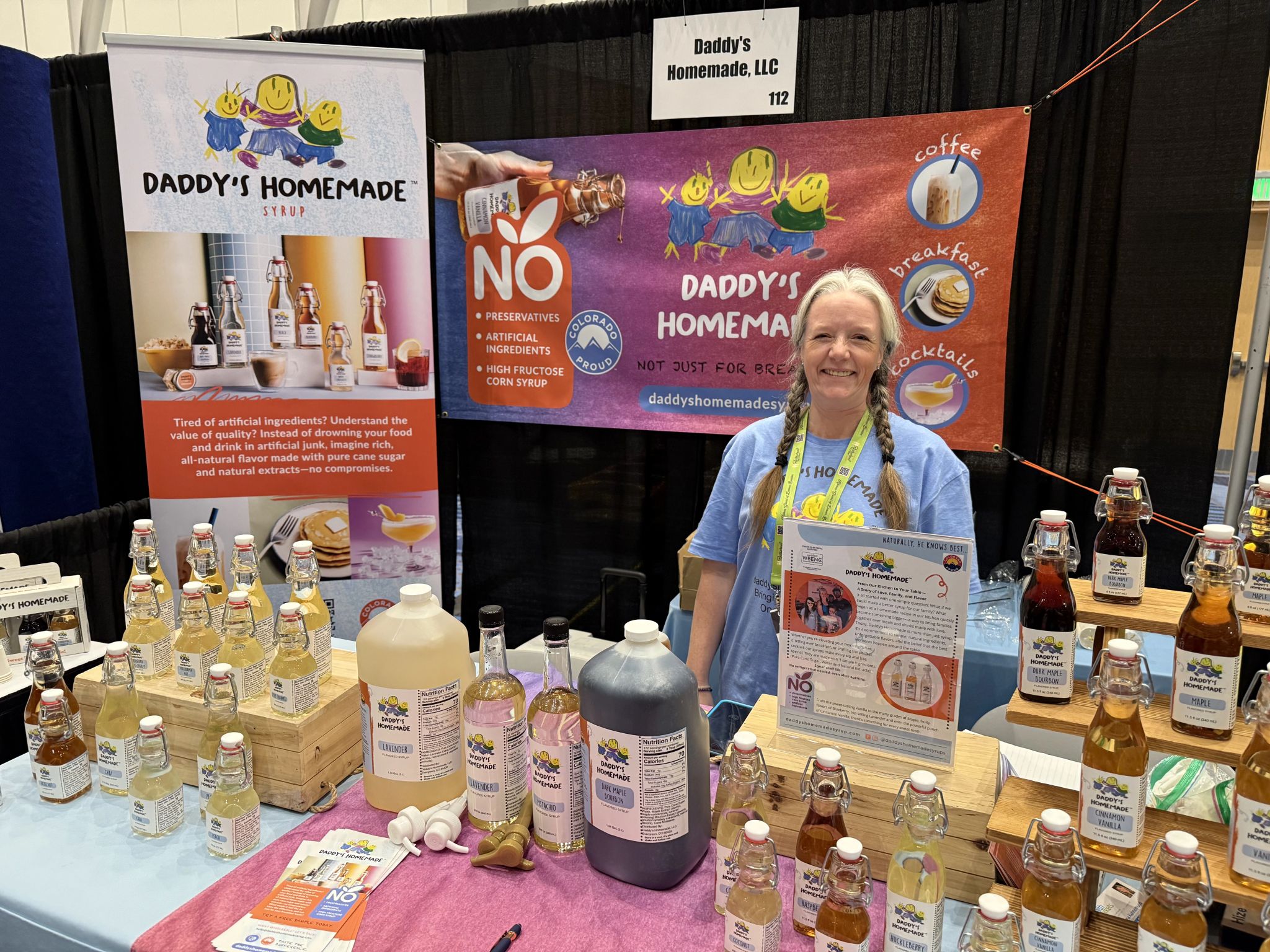 Amber Burr standing at a table in a booth with Daddy's Homemade Syrup products