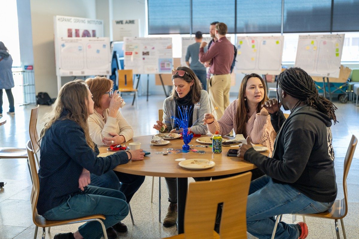 Folks gathered around a table and chatting during an OER Celebration