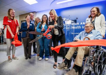 The Day Health Institute team surrounds Gina and Frank Day as they cut a red ribbon in front of the Interprofessional Simulation and Skills Laboratory