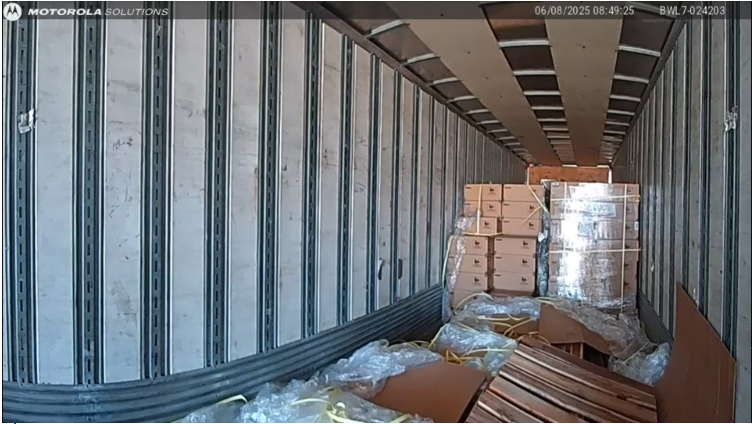 Inside the trailer of a semi truck with boxes stacked up and flattened boxes at the front.