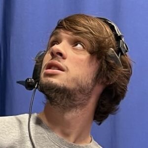 A young man with brown hair and a short beard wearing a headset