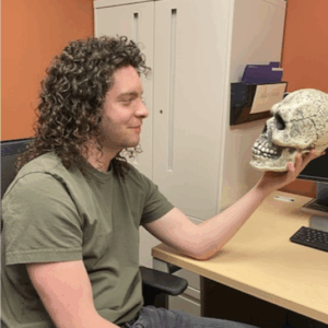 A young man with long curly hair holding a fake skull