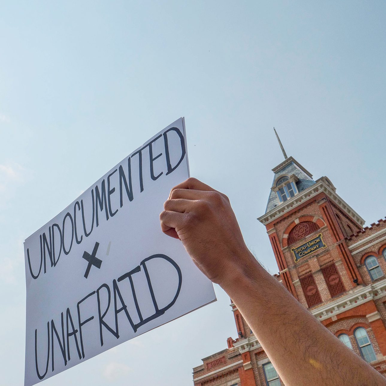 a hand holding a sign in front of the Tivoli that says Undocumented, Unafraid