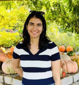 woman in black and white striped shirt standing in front of pumpkins and plants