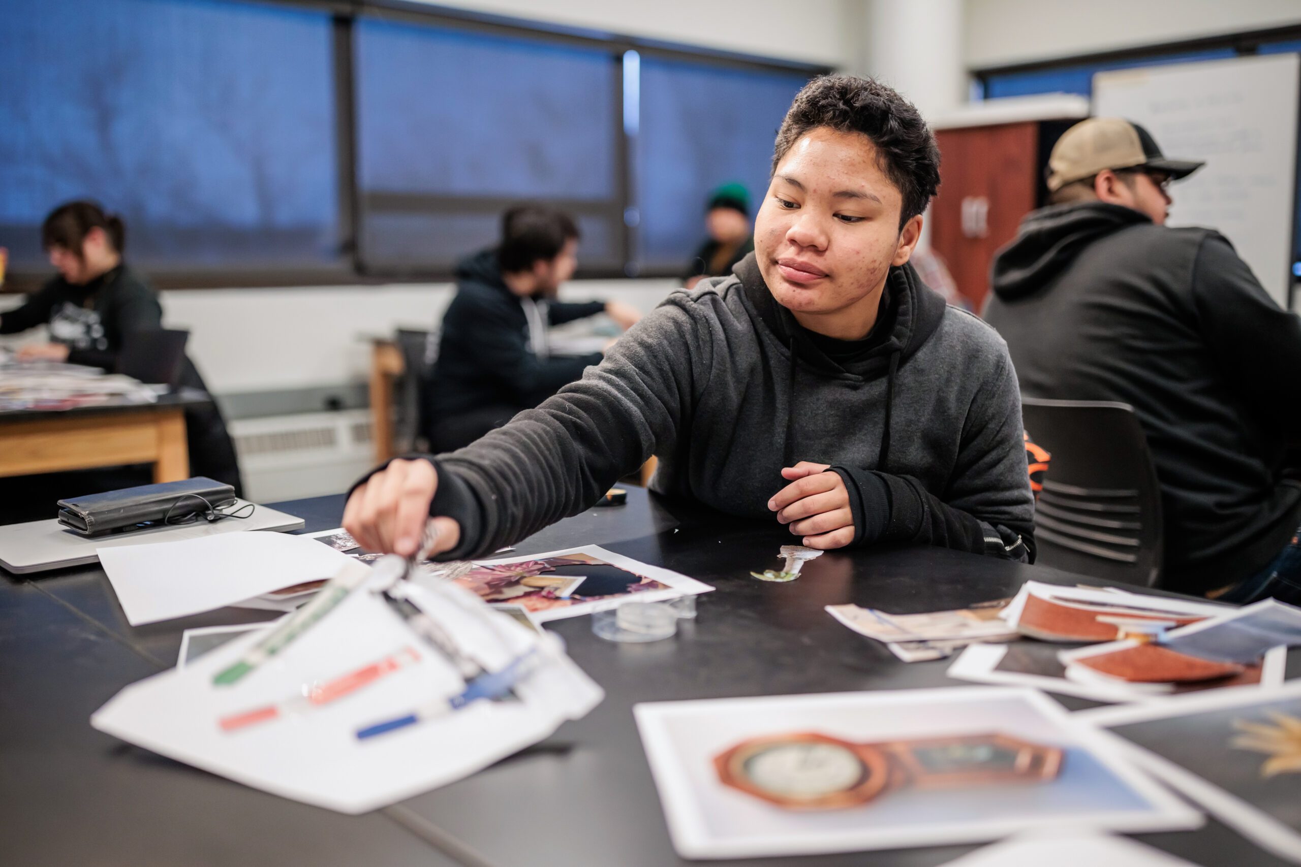 A student with short, dark hair sits at a table in front of a spread of pages with colorful images.