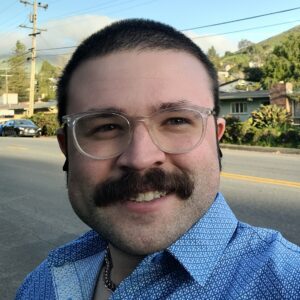 A young man with short brown hair and a mustache wearing glasses