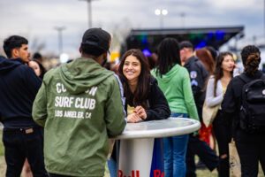Two students having a conversation at the Roadrunners After Dark concert by a Red Bull table.