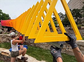 Interns place a series of rainbow painted geometric wood shapes.