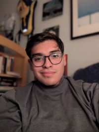 Neldo wearing gray turtle neck and black rimmed glasses