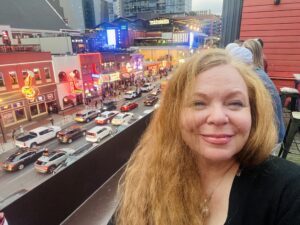 Downtown Nashville on left hand side, Kit, on right hand side smiling. Red hair and black top.
