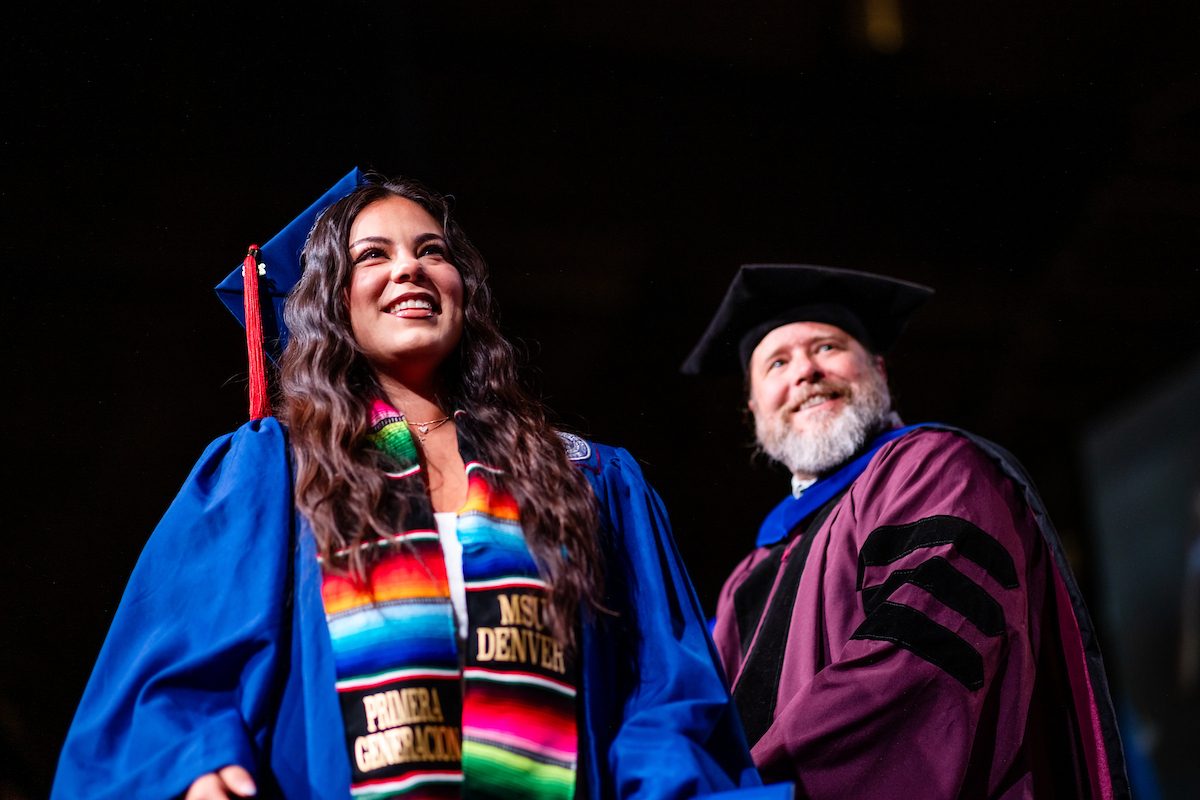 MSU Denver student walking across graduation stage with faculty smiling