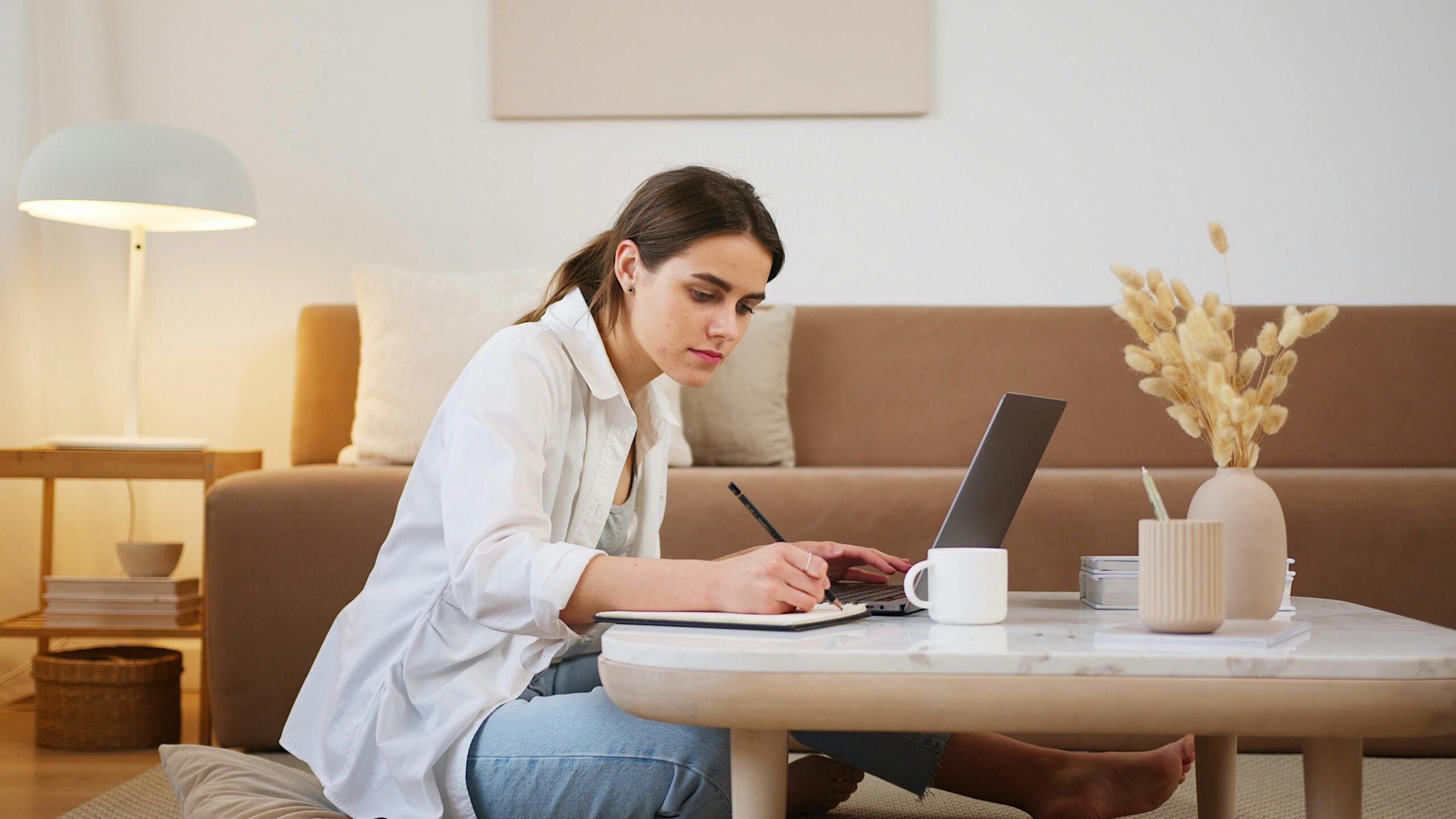 A person in a white shirt writing with a pencil and paper on a table.