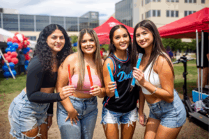 four students standing outside together and smiling while holding popsicles
