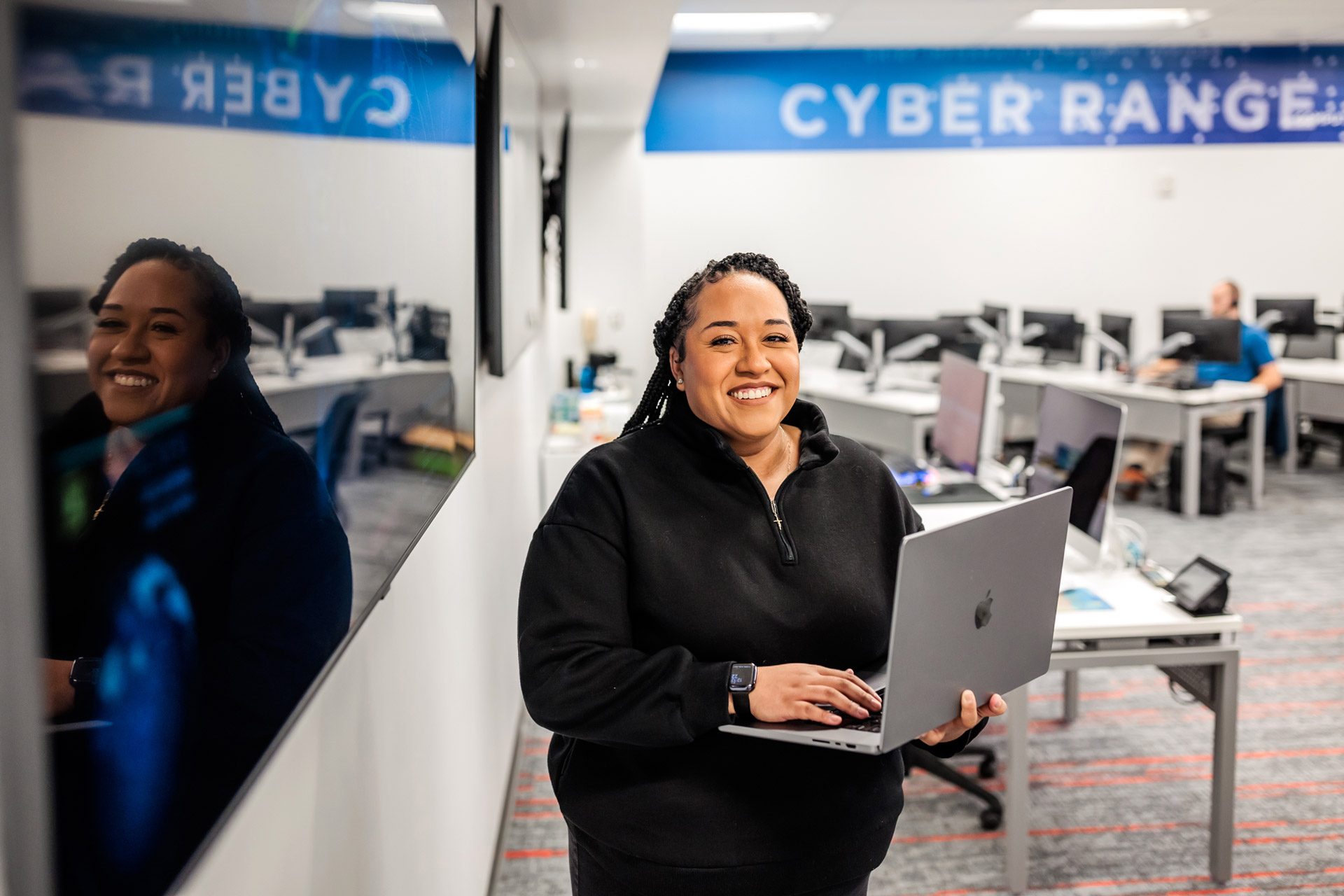 Alumna Dominique Niquete smiling and standing in a cybersecurity room