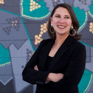 Woman standing in front of art mural. She is wearing all black and has medium brown hair. 