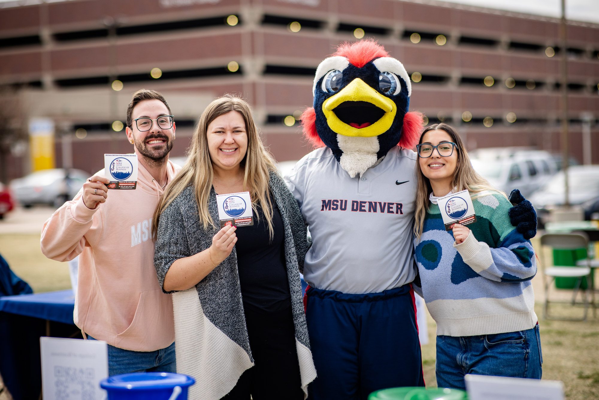 Three students standing with Rowdy holding up College of Business stickers on MSU Denver Day of Giving 2025