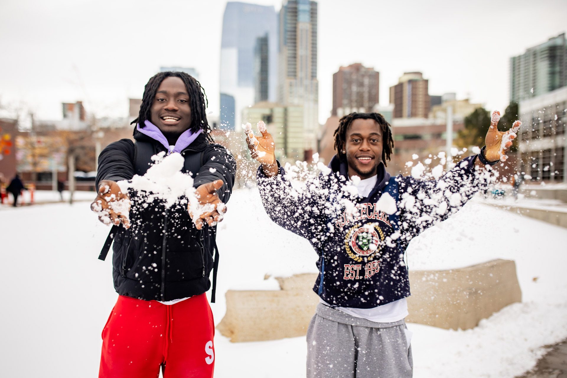Two students on the first day of spring classes in 2025 smiling and tossing snow towards the camera