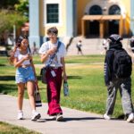 Two students walking across campus with a green background