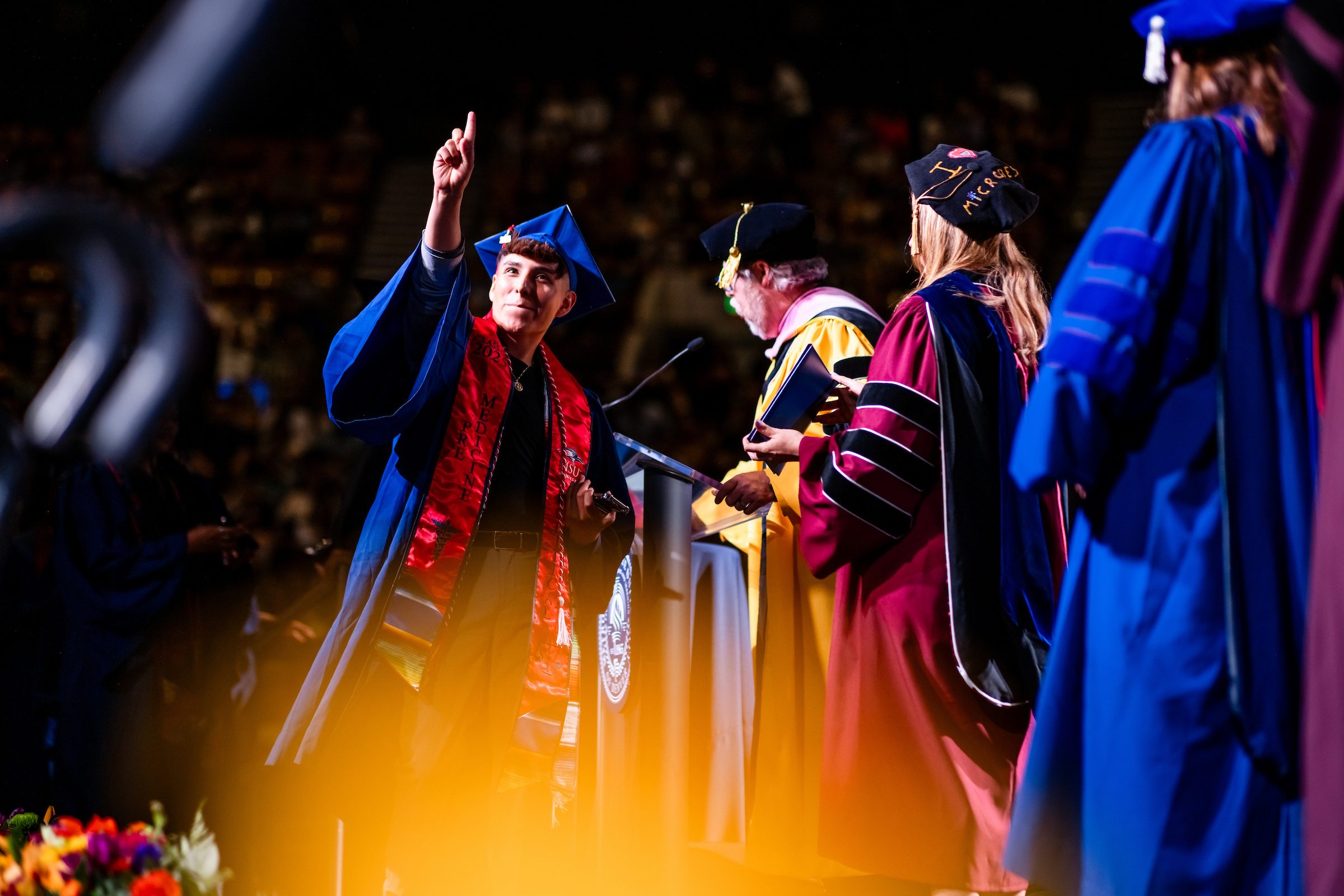 Student pointing up in celebration while holding up diploma