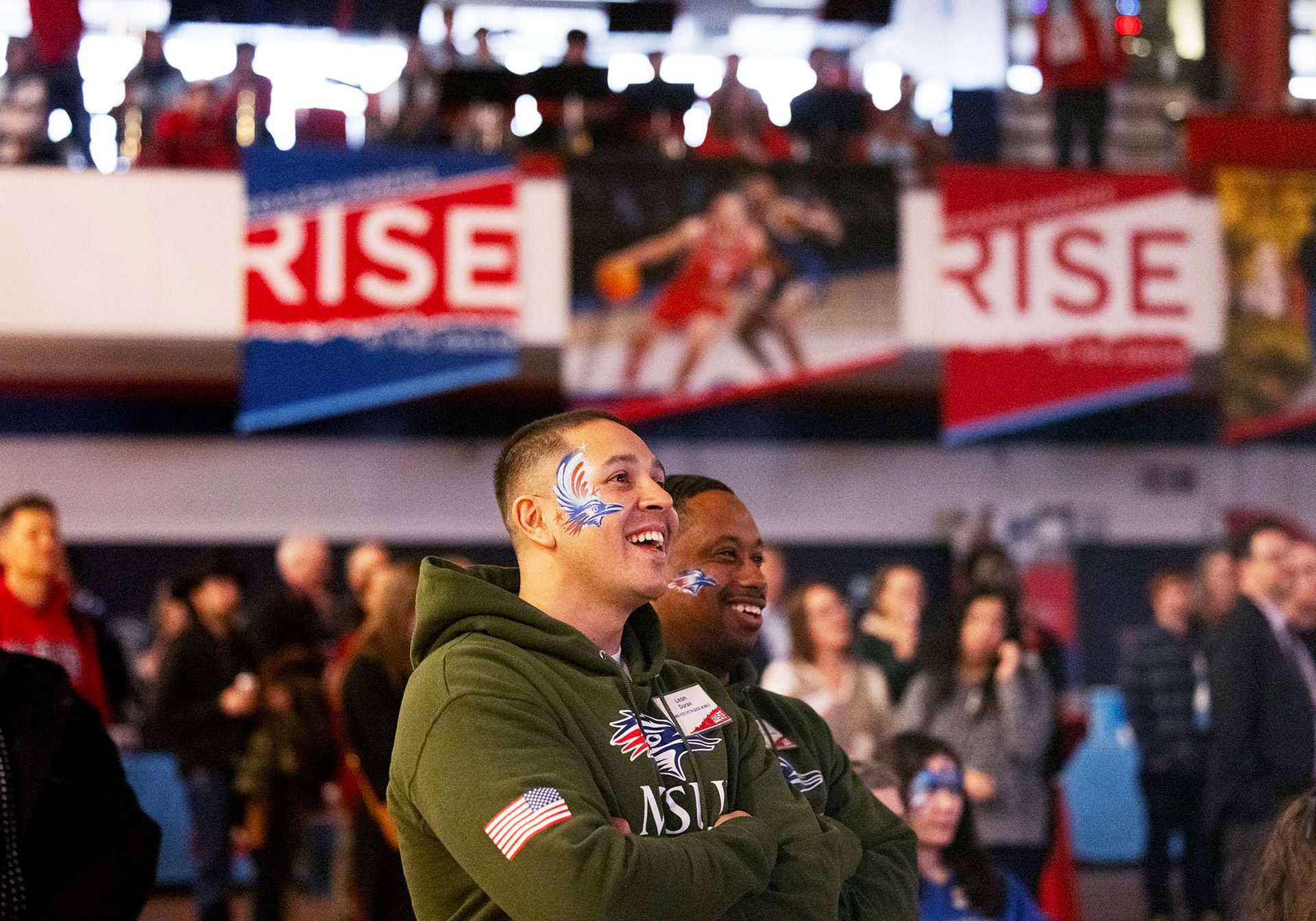 Alums Leon Duran and Jameer Fitch laugh as they listen to a speaker at the Roadrunners Rise campaign launch event. They are wearing their military green MSU Denver sweatshirts