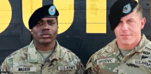 Two US military members standing in front of a black wall