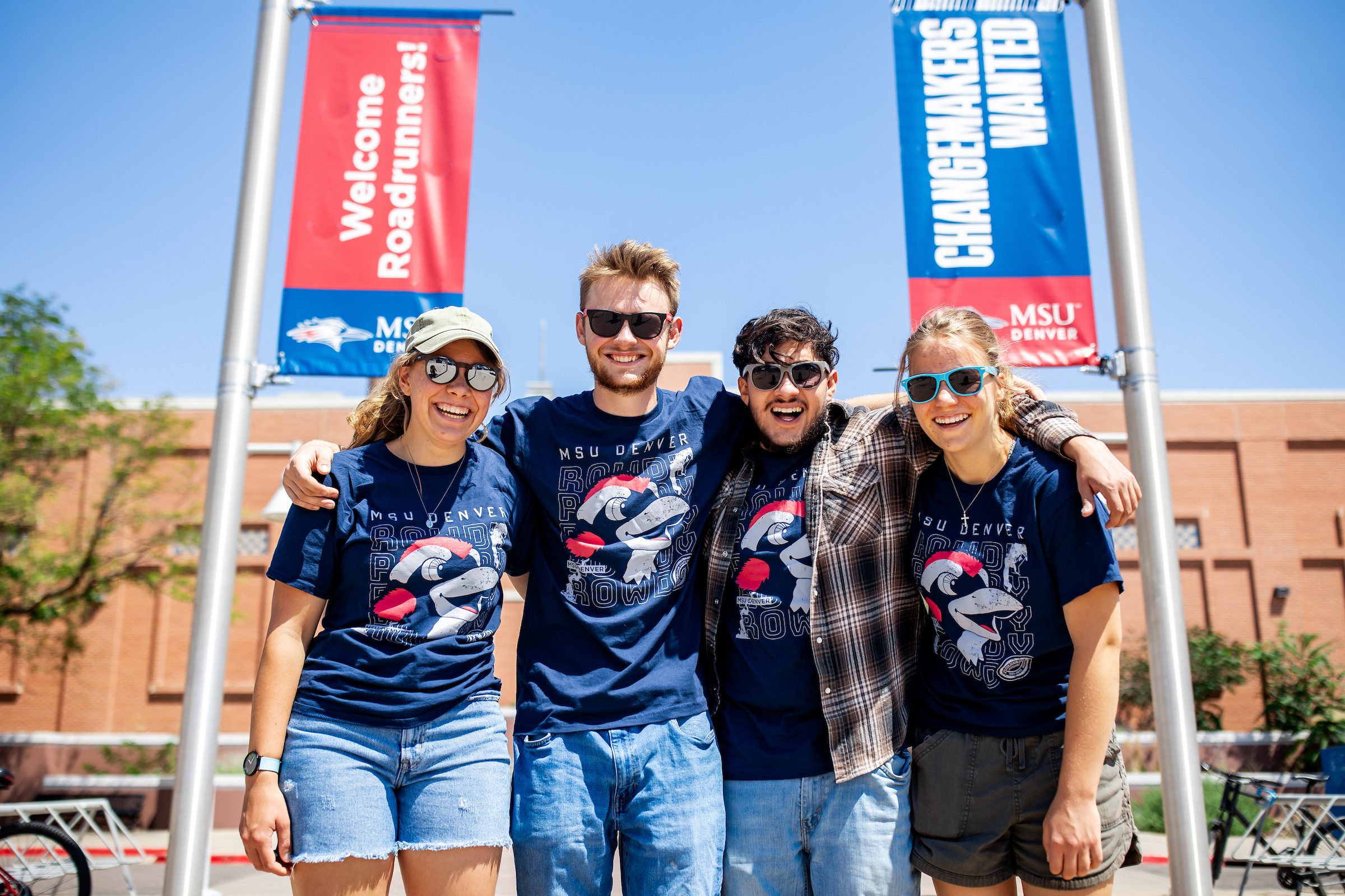 Four students smiling in the son infront of a building