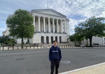 A young man stands in front of the Longworth House buidling in Washington, DC.