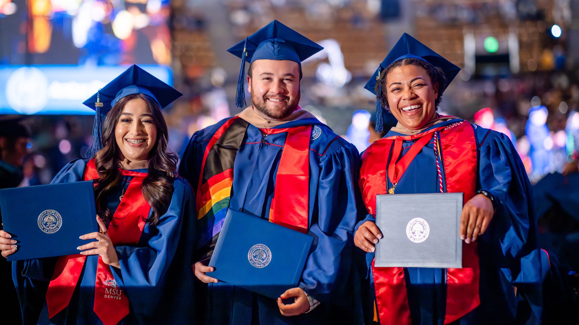 Three graduates smiling and holding their diplomas at commencement