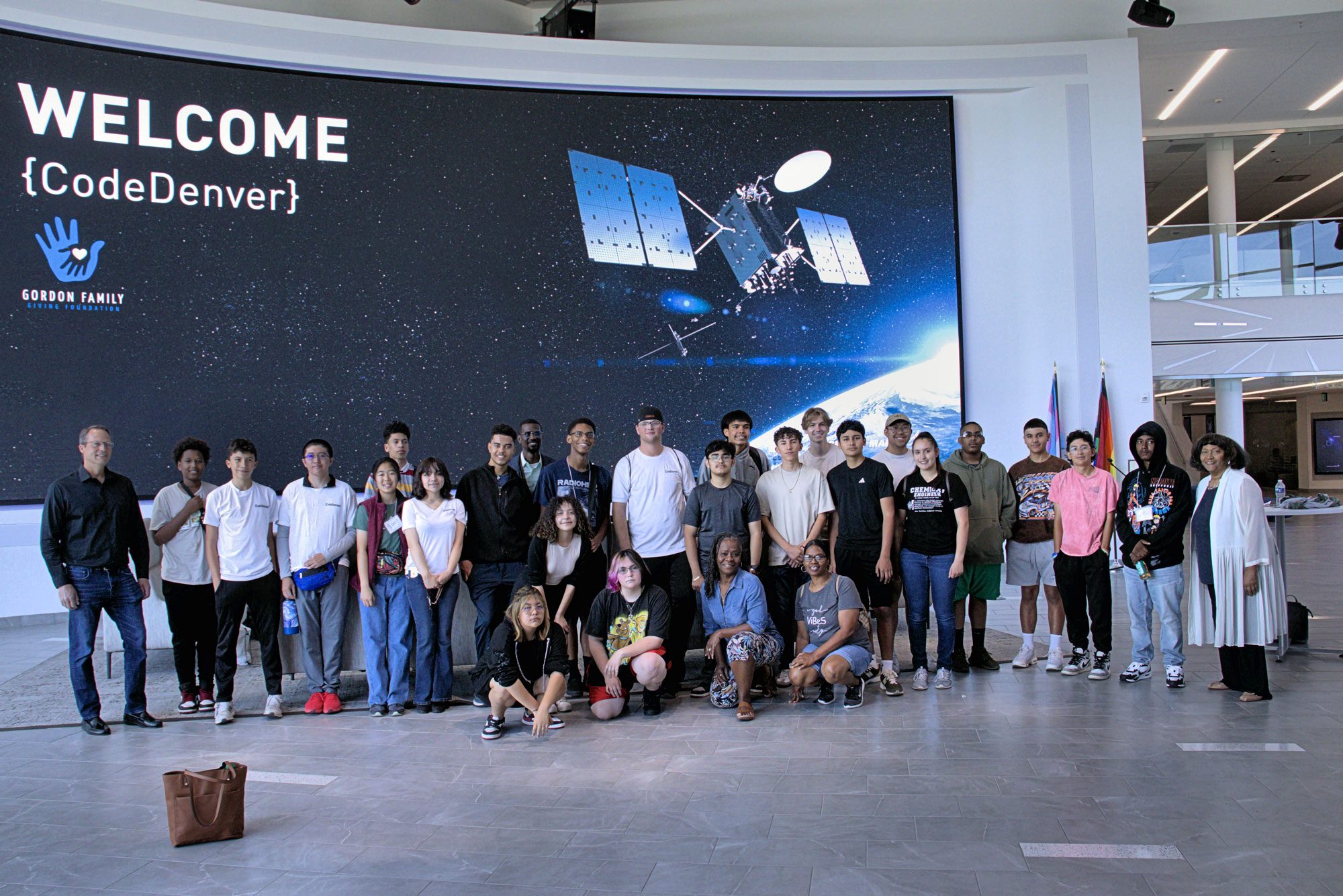 A group of high school students standing in front of a Welcome CodeDenver sign with a satellite on it