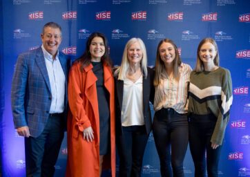 Three MSU Denver students standing for a photo with Rob and Molly Cohen in front of a Roadrunners Rise backdrop