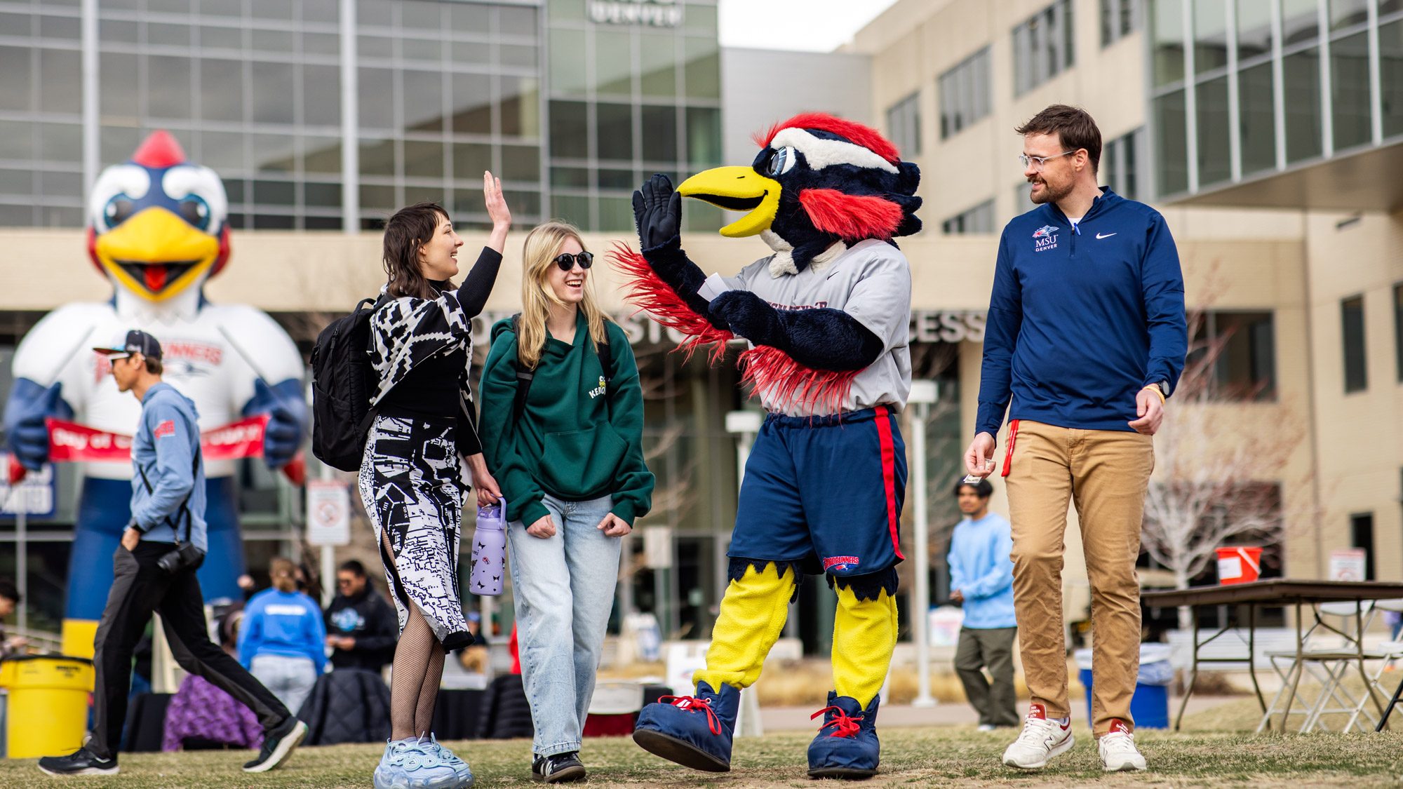 Two students high-fiving Rowdy in front of JSSB on the grass