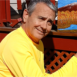 Nick Manely wearing a yellow shirt and red lattice in the back ground