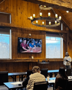 Andrew S. teaching a TIPS training to a group of students. A tv is playing a demonstration to the group in the background.