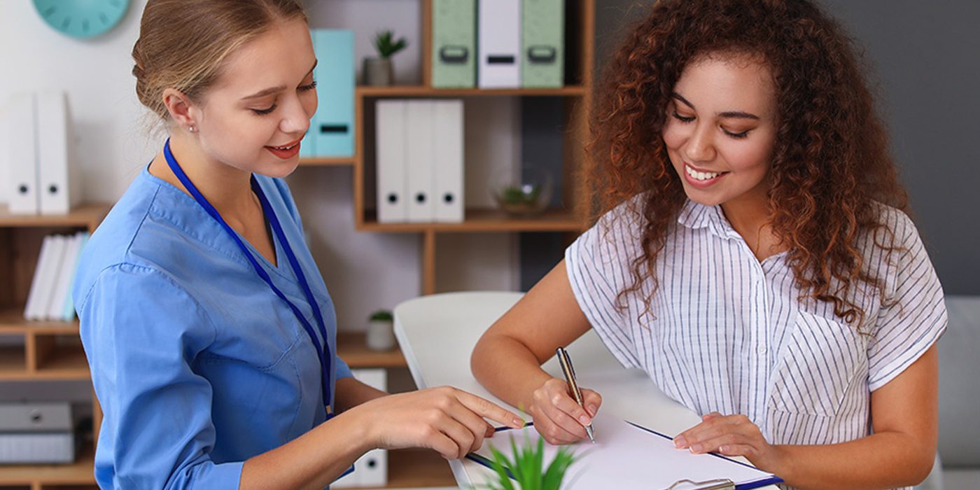 Two women in medical office and one is writing on a clipboard