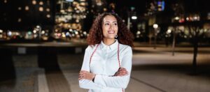 Student wearing graduation cords standing in front of city buildings at night