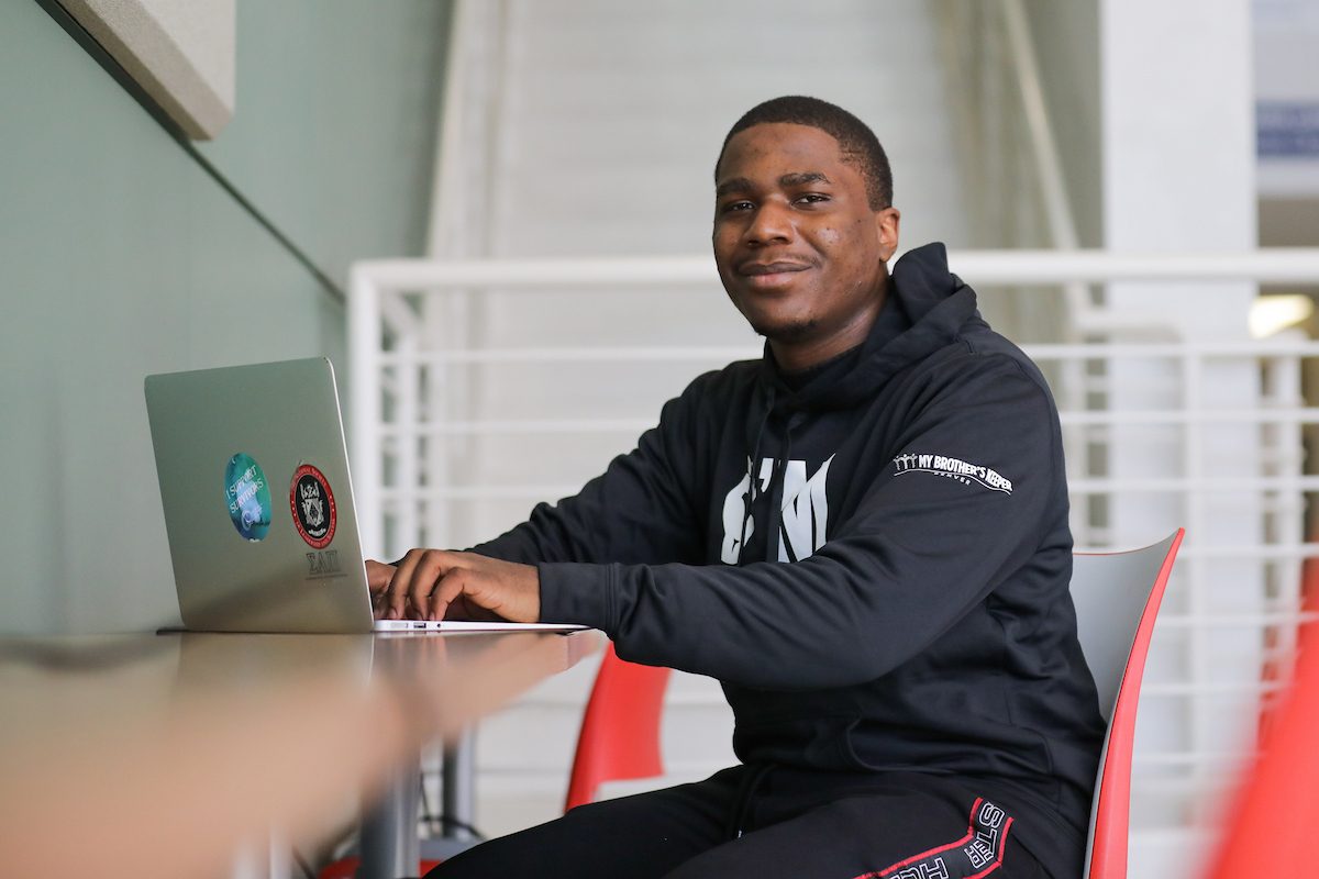 Student typing on hit laptop in the middle of a lobby