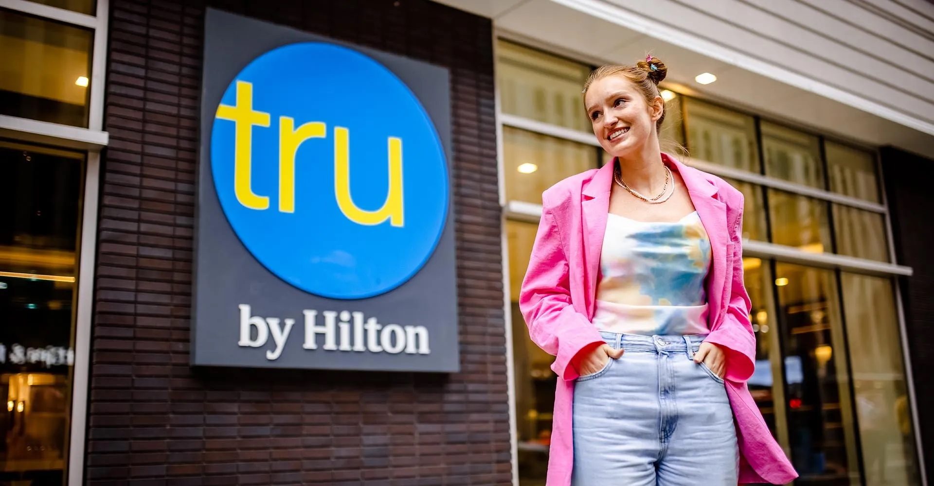 Hospitality Leadership student standing by the tru by Hilton hotel sign