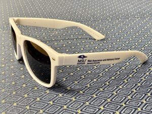 RAA center logo on the arm of a pair of white sunglasses on a navy blue and gold diagonal background