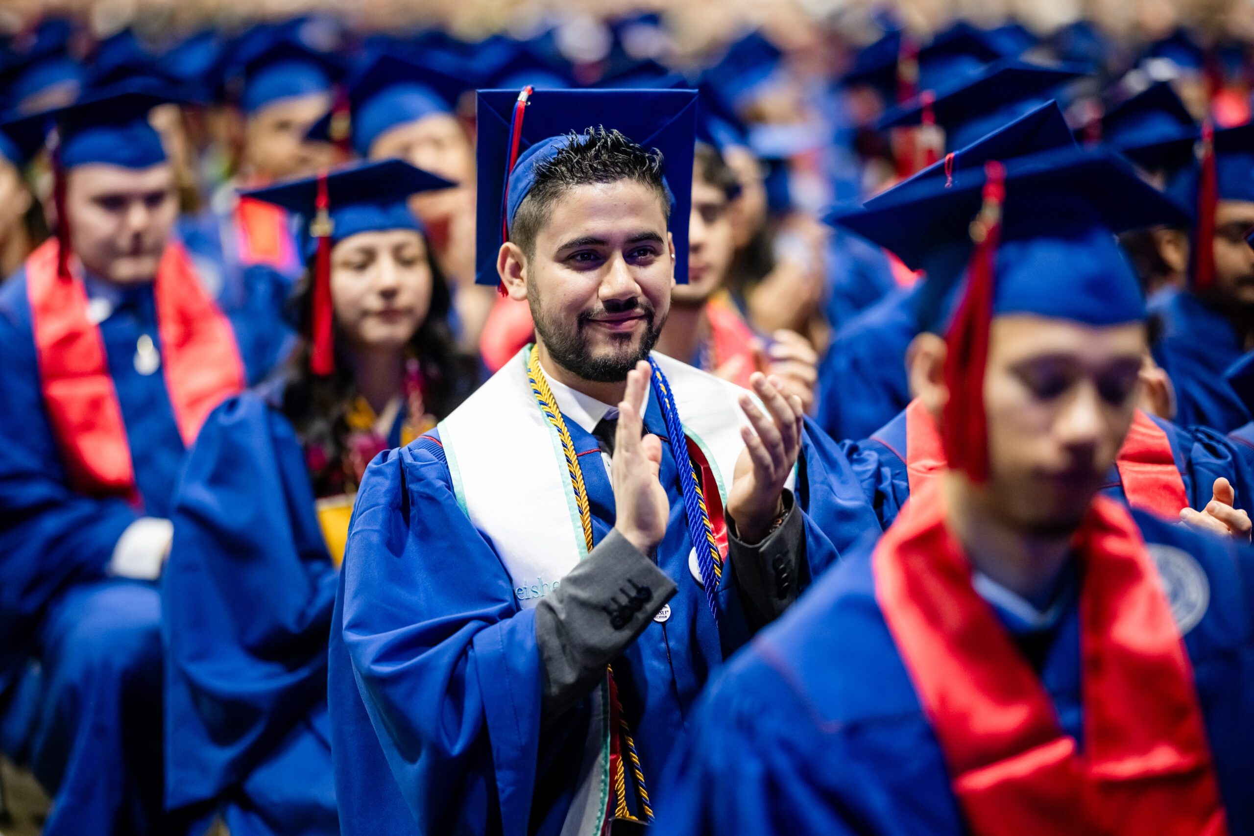 Fall '25 Commencement Ceremony - accounting student clapping while sitting amongst peers all in regalia
