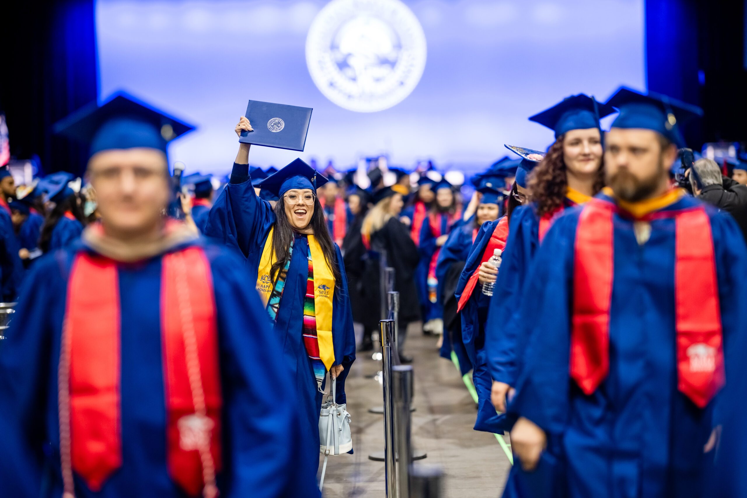Fall '25 Commencement Ceremony - MPAcc grad, Kiana, holds up diploma cover as grads during recessional