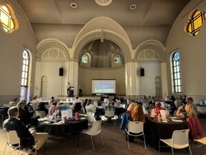 packed room with audience looking at 2 presenters on stage at the Fall '25 RAA center event