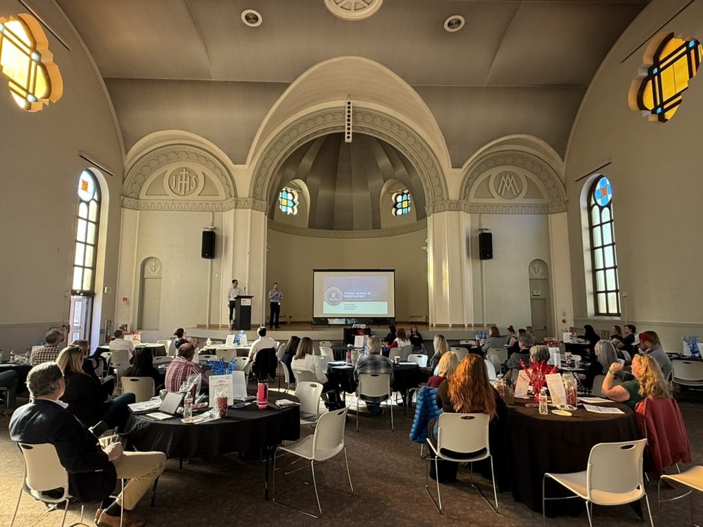 packed room with audience looking at 2 presenters on stage at the Fall '25 RAA center event