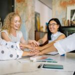 Women sitting at a table shaking hands.