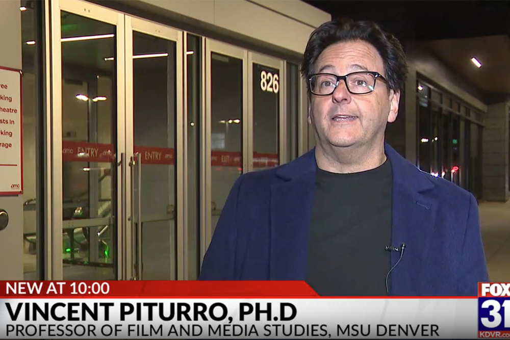 Dr. Vincent Piturro speaks during a nighttime television interview outside a theater entrance. On-screen text reads 
